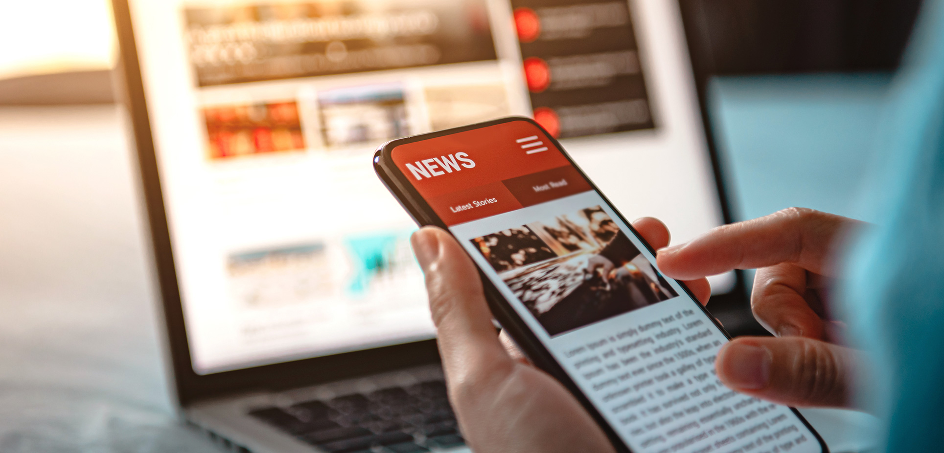 Ruka drží mobil so správami, v pozadí je rozmazaný notebook so zobrazenými správami.
