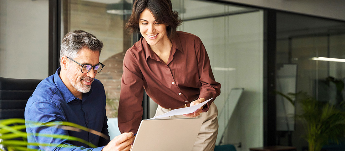 muž a žena diskutujú nad otvoreným laptopom v kancelárii, žena drží papiere